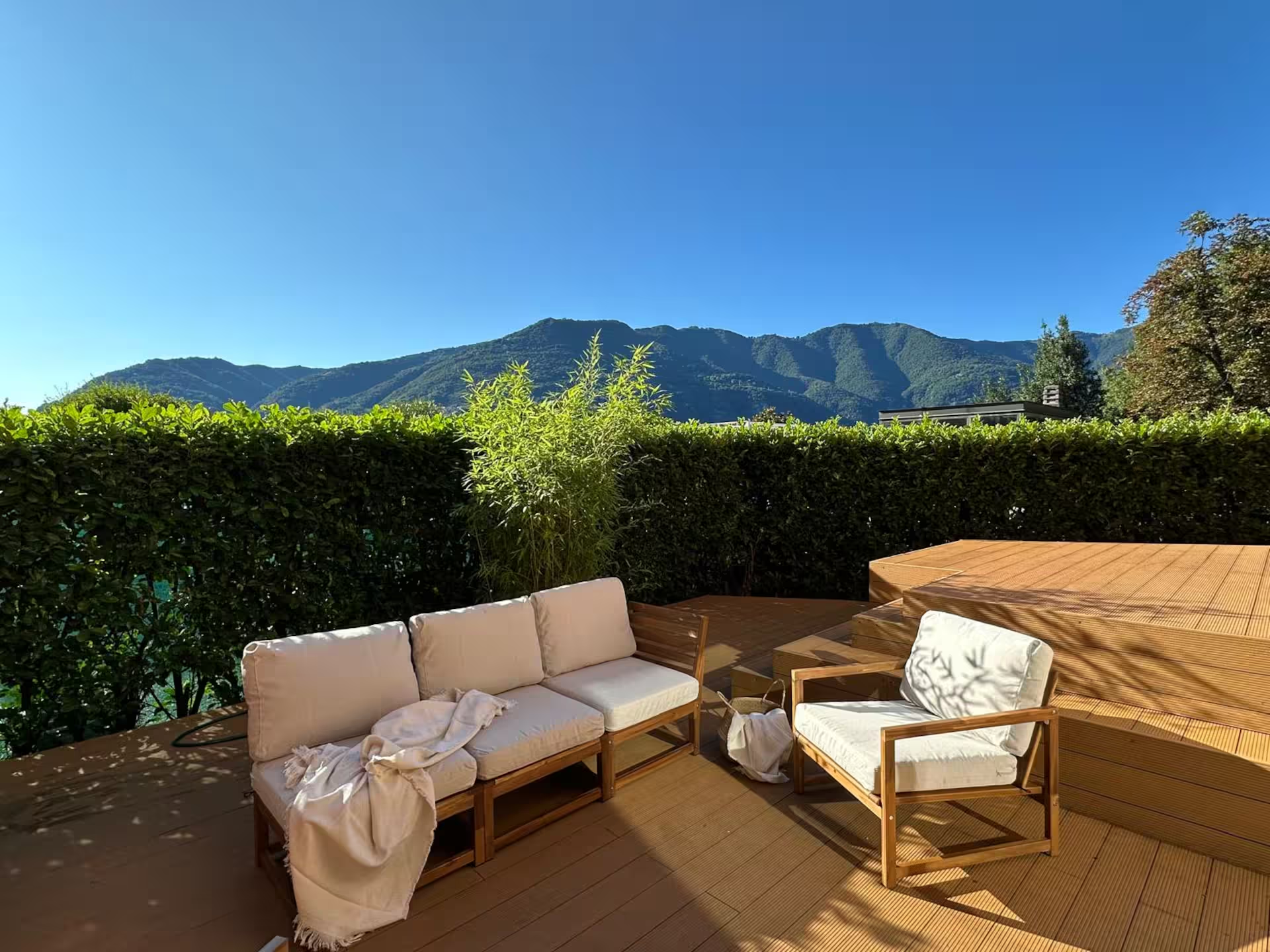 Privéterras met teakhouten meubelen, bergzicht en natuurlijke haagafscherming